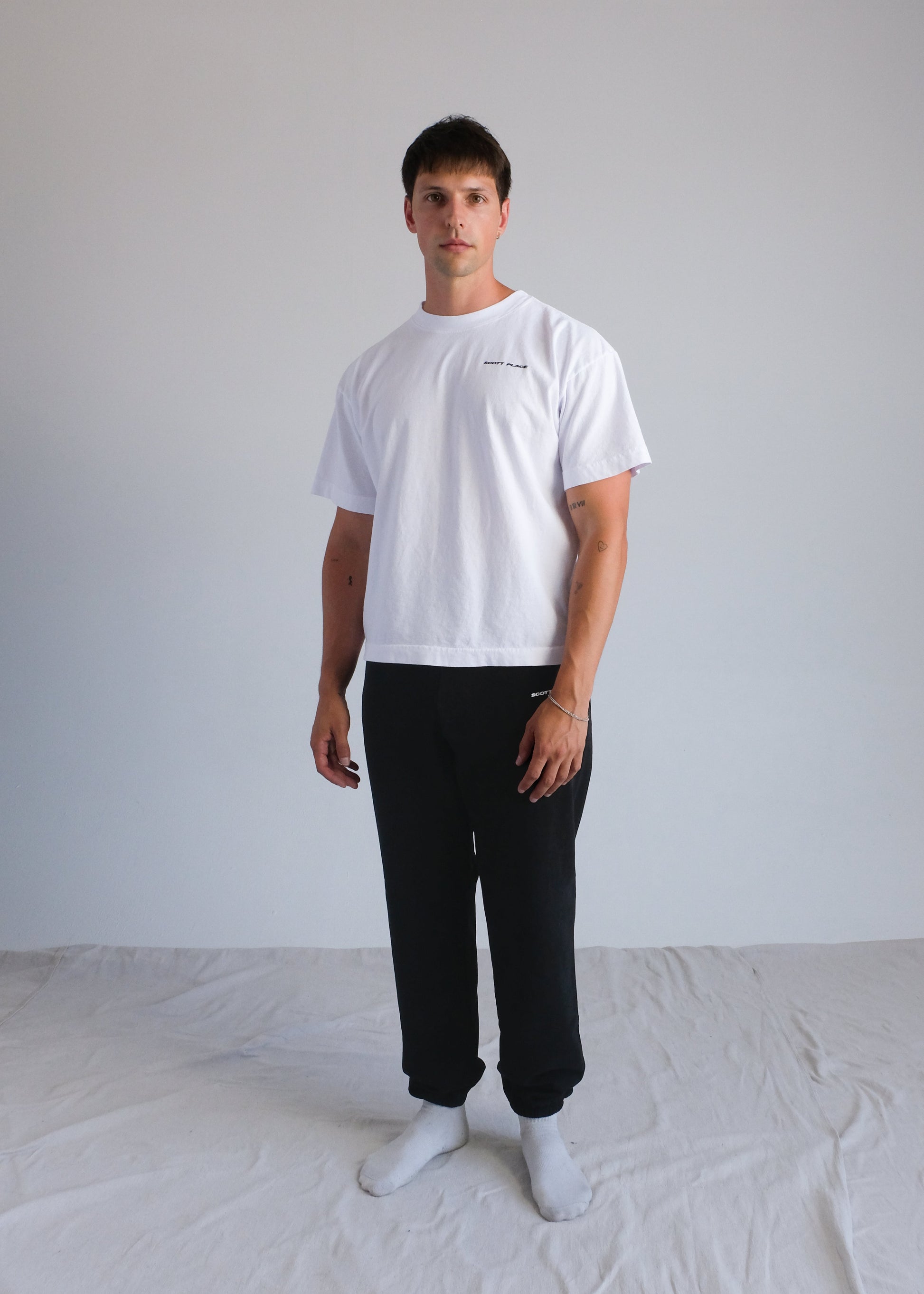 Man wearing a white t-shirt and black pants standing against a plain background