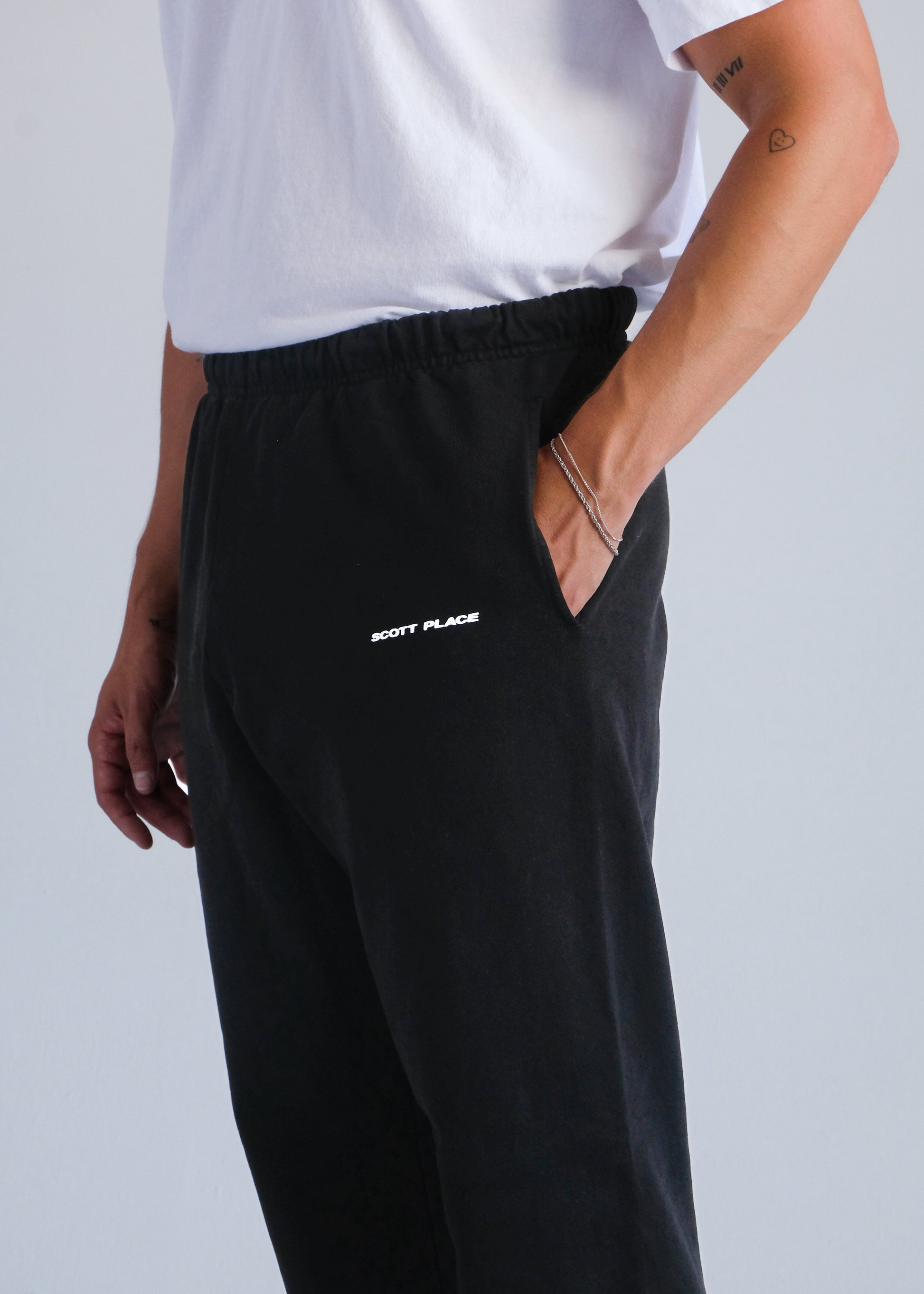 Person wearing black pants with a brand logo on a light gray background