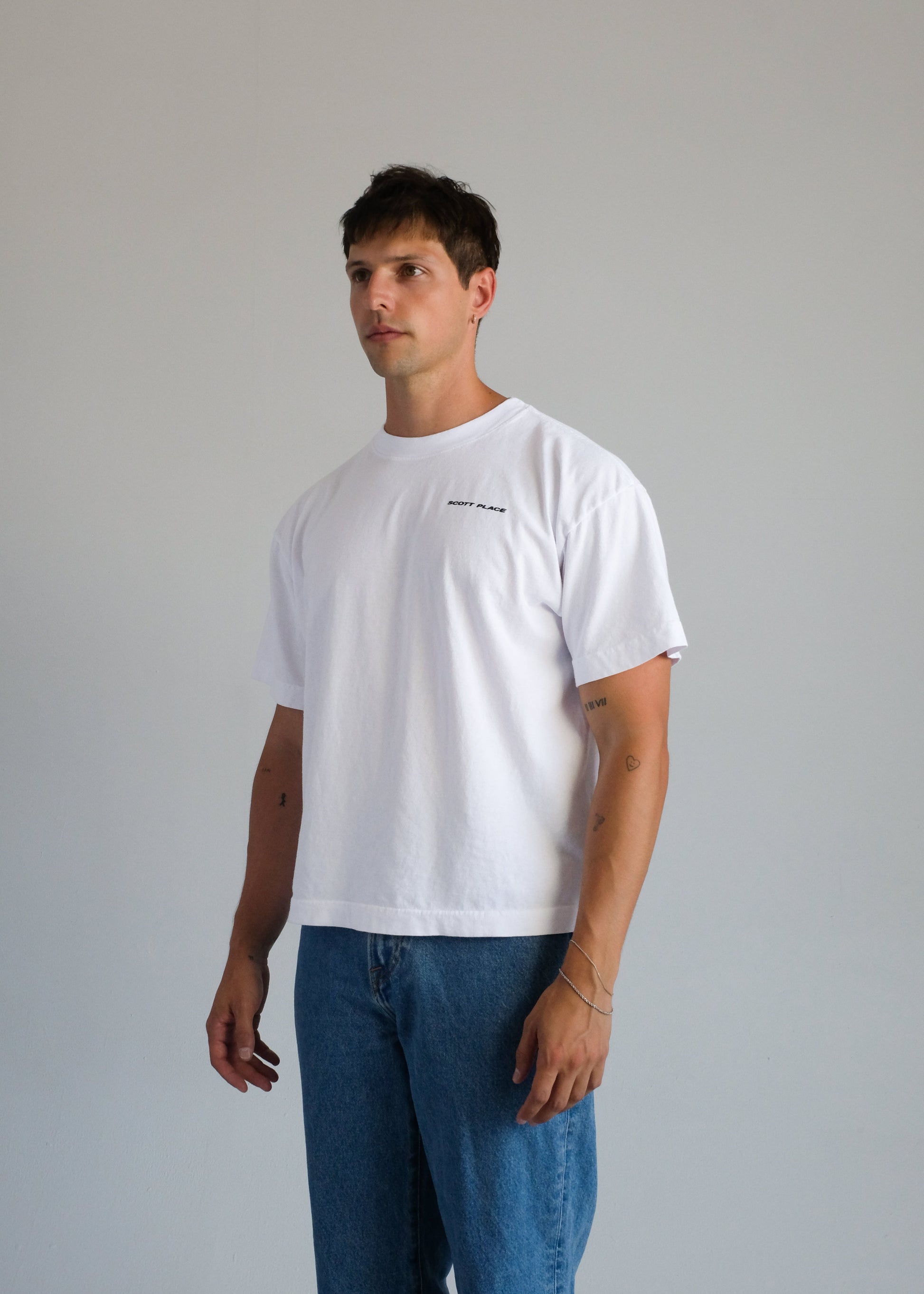 Man wearing a white t-shirt and blue jeans against a plain background