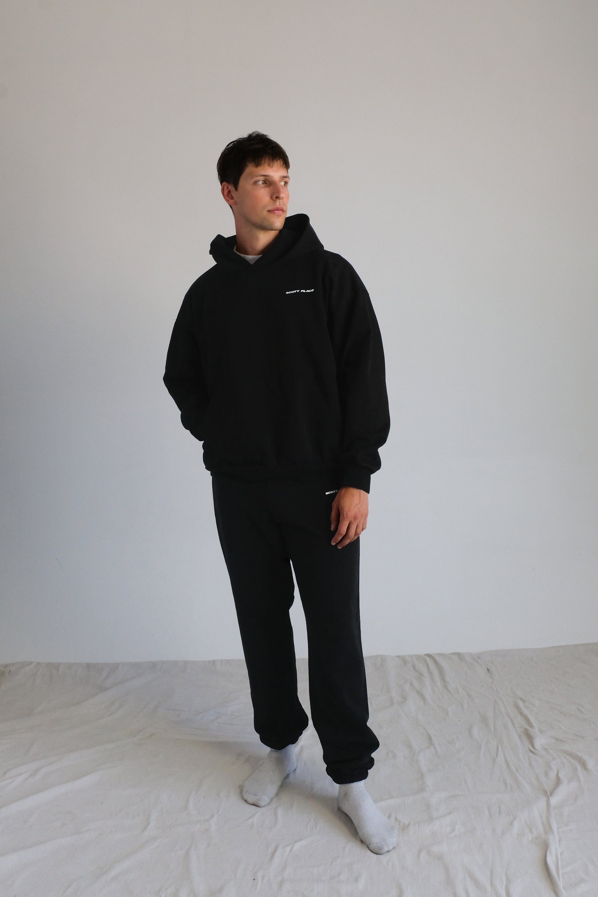 Person wearing a black hoodie and pants standing against a white background