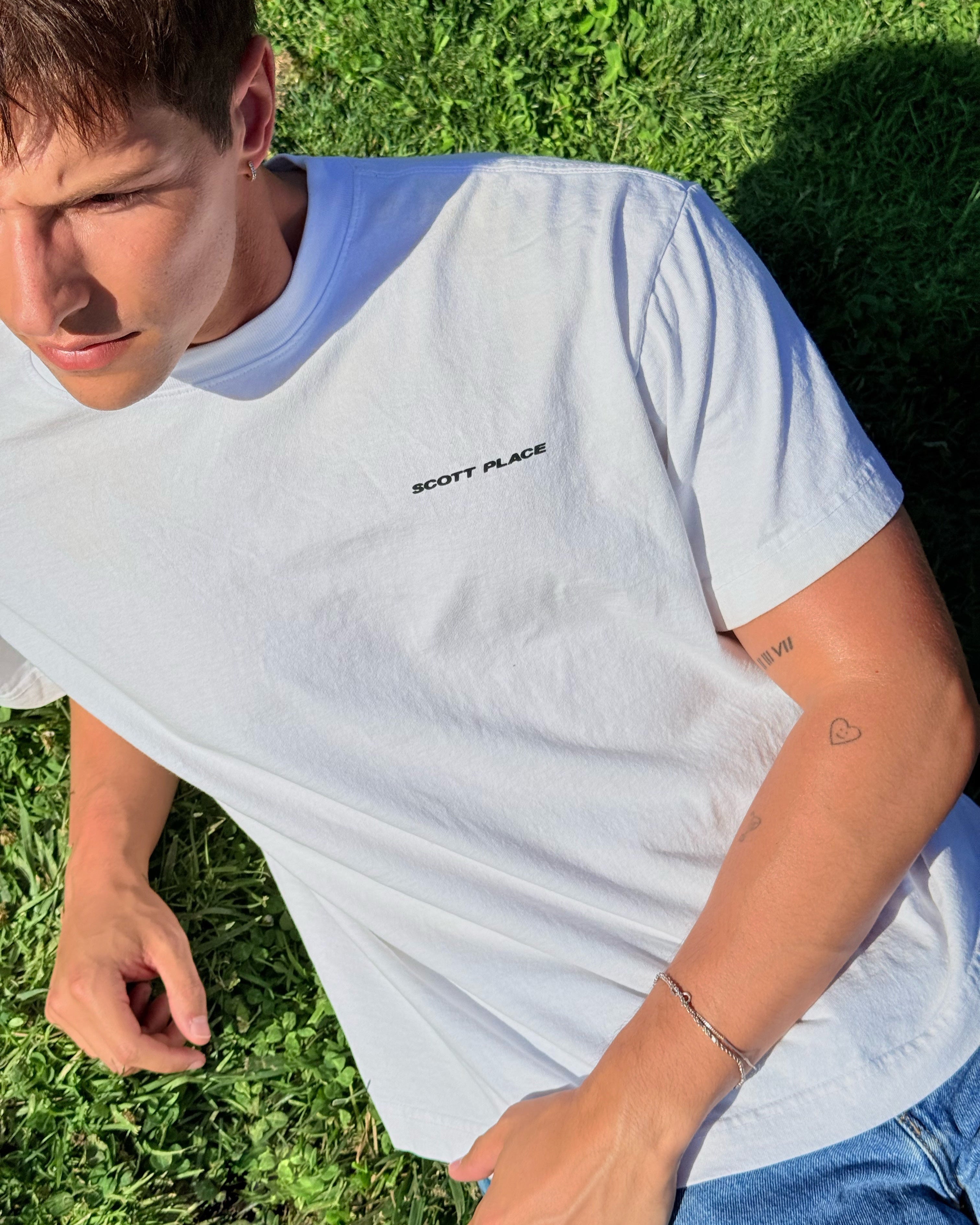 Person wearing a white t-shirt with 'Scott Place' logo on grass