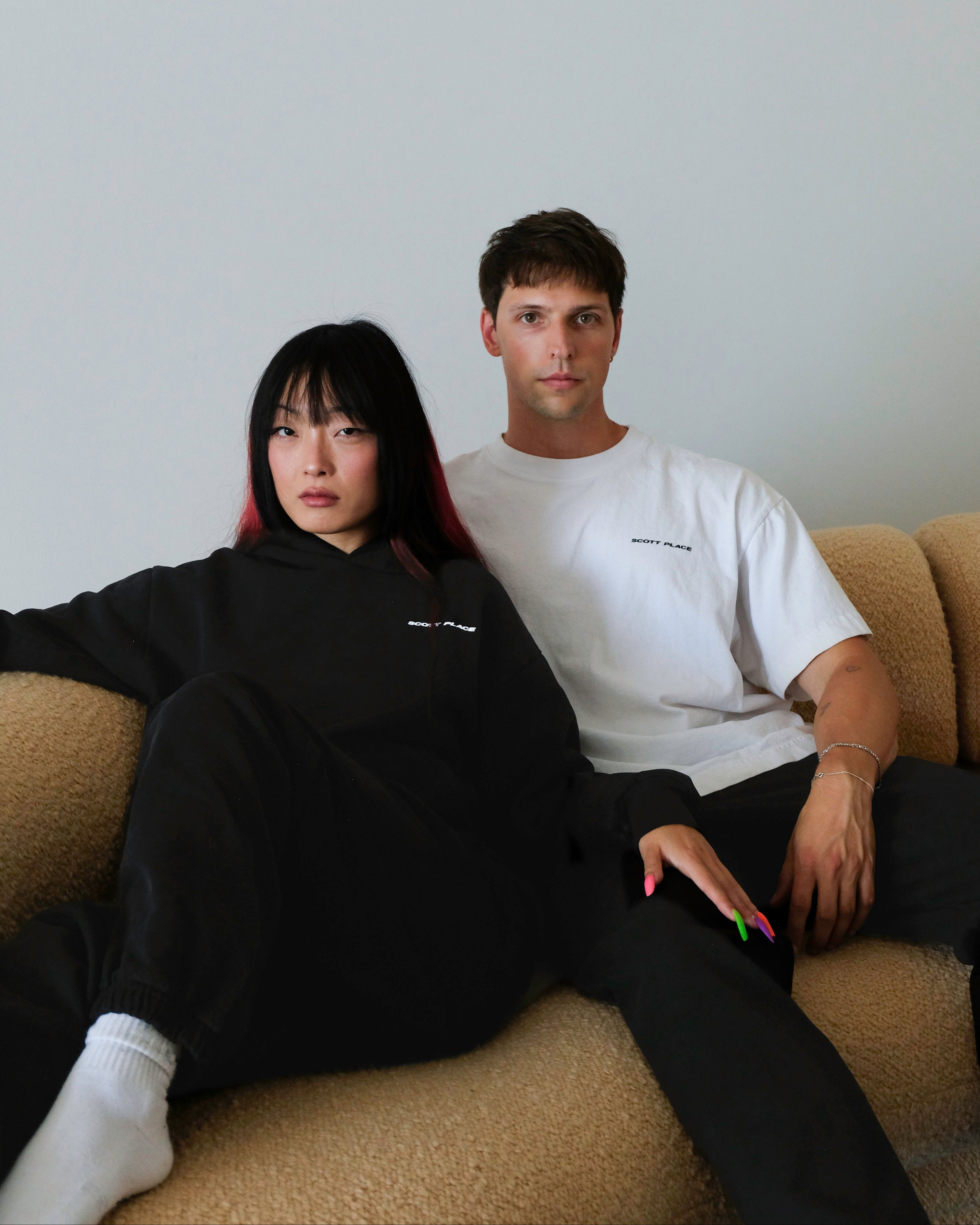 Two people sitting on a couch against a plain wall.