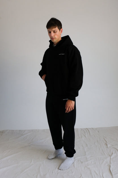 Person wearing a black hoodie and pants with white socks on a plain background