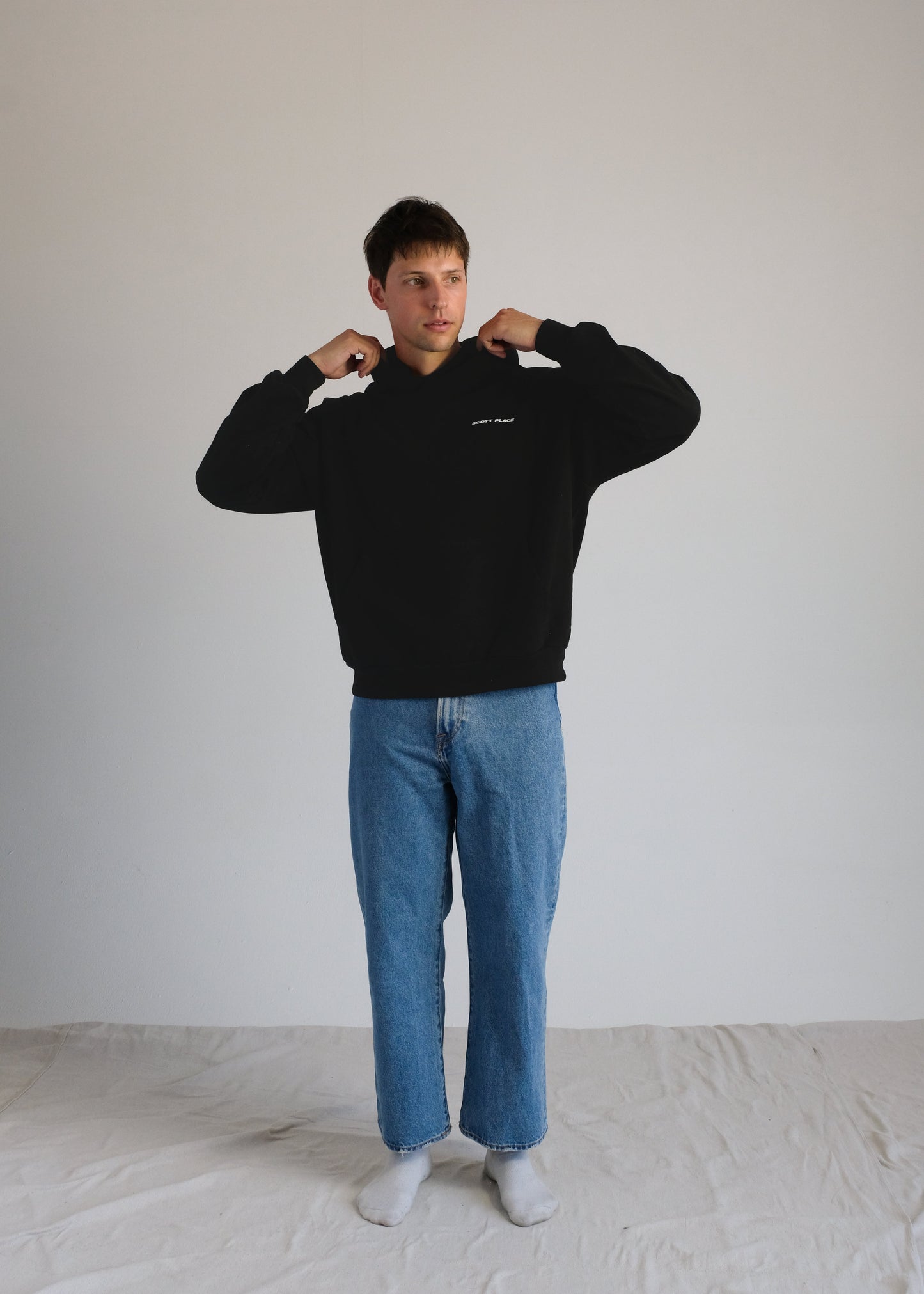 Person wearing a black sweatshirt and blue jeans standing against a plain white background