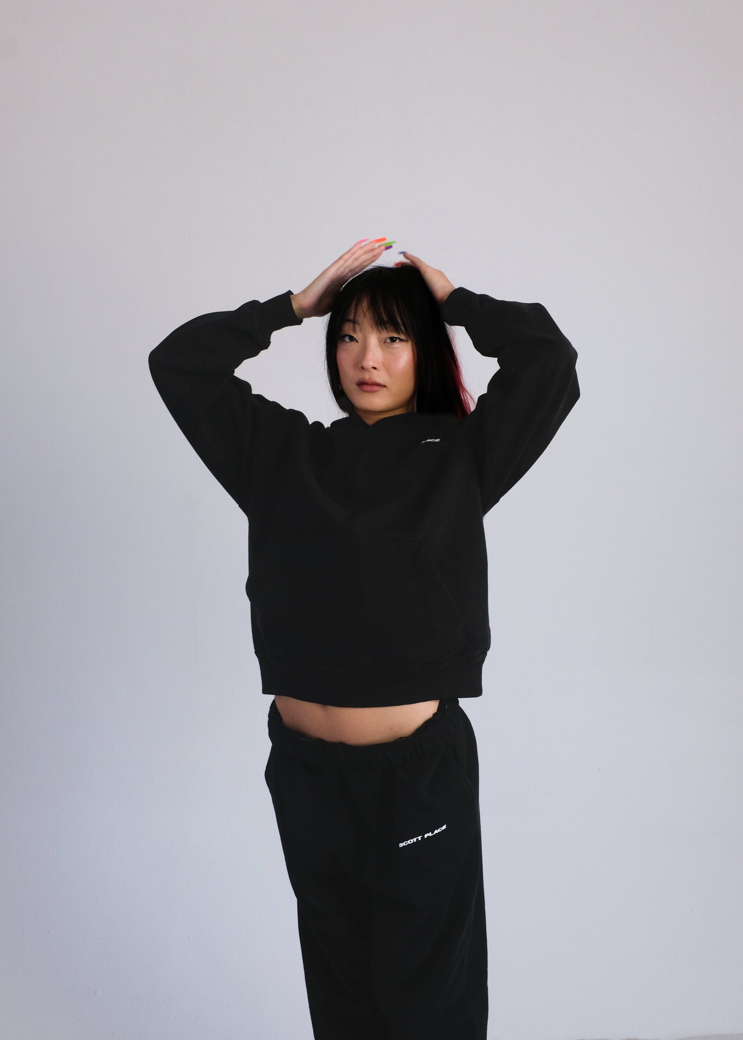 Person wearing a black hoodie and pants with a logo on a plain background